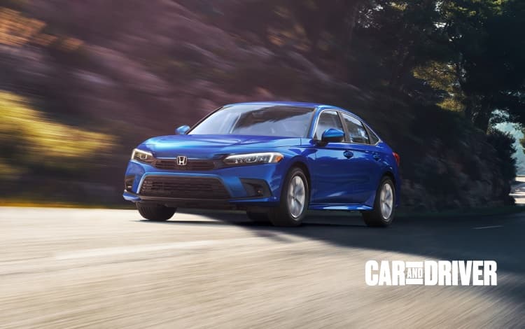 Passenger-side profile view of the 2021 Honda Civic Touring Sedan in Lunar Silver Metallic shown on a rural road in front of autumnal trees.