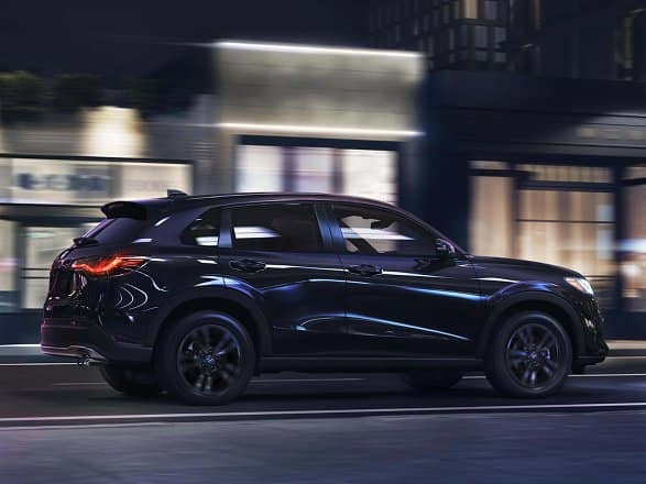 2027 Honda HR-V Sport in Crystal Black Pearl profile view driving through an urban street (Subcompact Crossover SUV).
